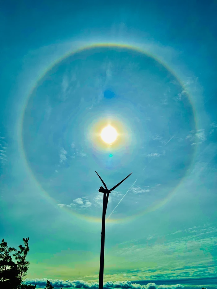 Solar halo around the sun with a wind turbine silhouette in the foreground and a blue sky backdrop.