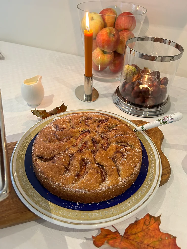 Homemade apple cake on a table with lit candle, fresh apples, and grapes.