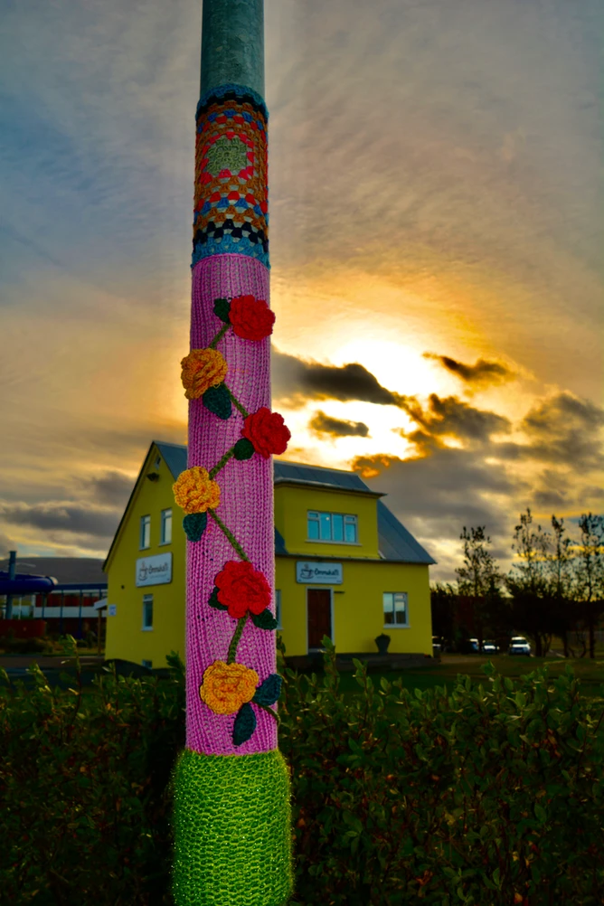 A lamppost covered with colorful knitwork against a sunset sky.