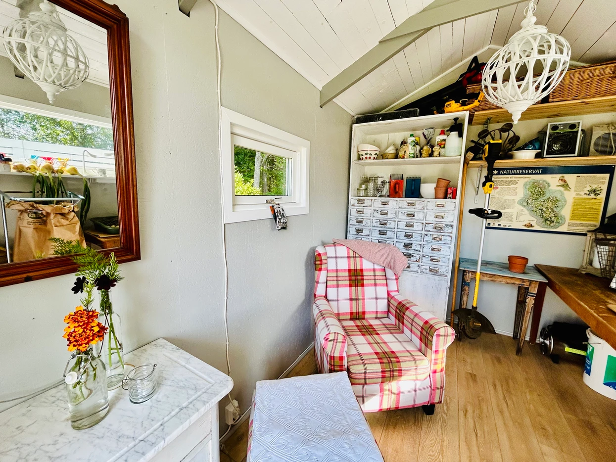 Cozy room with a plaid chair, white pendant light, and a shelf full of items.