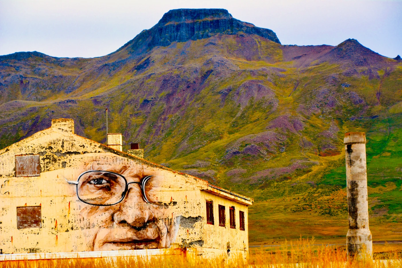 Abandoned building with a chimney in the foreground and a mountainous landscape in the background.