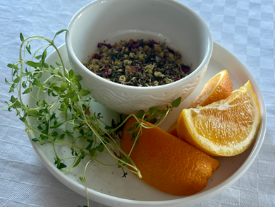A white bowl filled with herbs sits on a white plate, surrounded by fresh thyme sprigs and two orange wedges. The plate is set on a checkered white tablecloth.